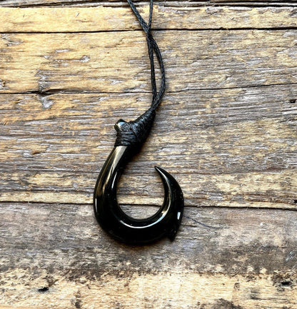 Black jade fish hook pendant displayed on rustic wooden surface with a knotted black cord above