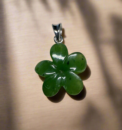 Green jade Forget Me Knot flower pendant with four-petaled petals and silver bail on beige backdrop.