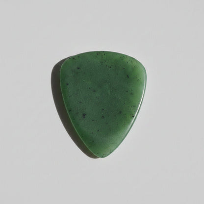 A satin finish green jade triangular guitar pick with natural speckles, resting on a grey surface