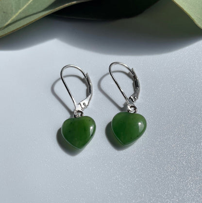 Close-up view of jade heart earrings with silver hooks on a white surface.