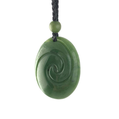 Close up of oval jade pendant with a spiral carving on a black braided cord and a green bead.