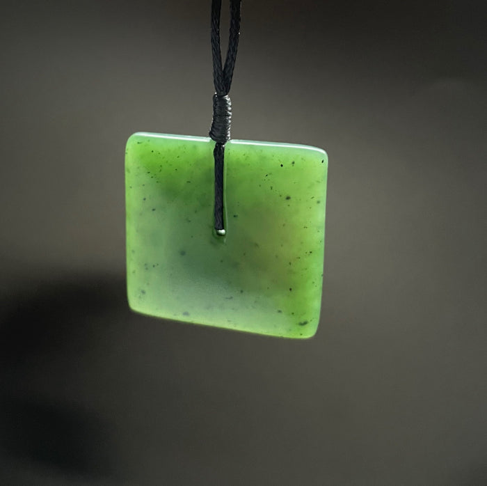 Close-up of a square green jade pendant with satin finish threaded on a black cord