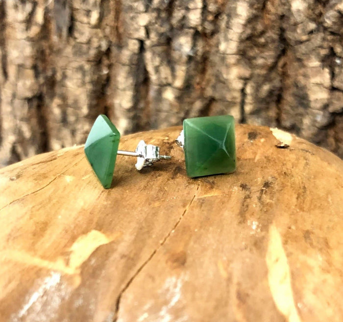 Two green jade square pyramid earrings with silver posts and butterfly backs on a wooden surface.