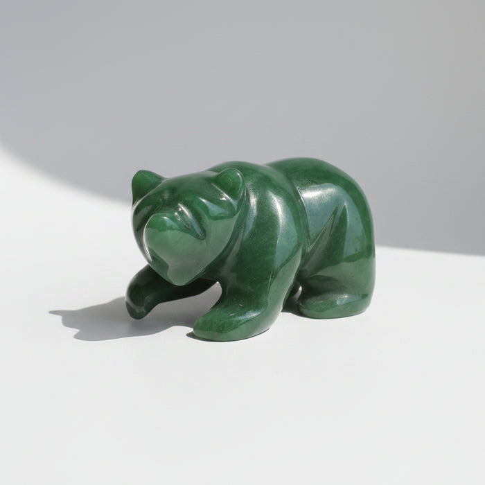 A polished green jade bear figurine resting on a wooden surface against a neutral gray background.