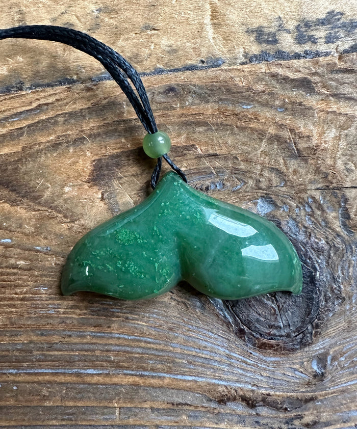 Jade whale tail pendant in green 39mm hanging on a black cord with a green bead.
