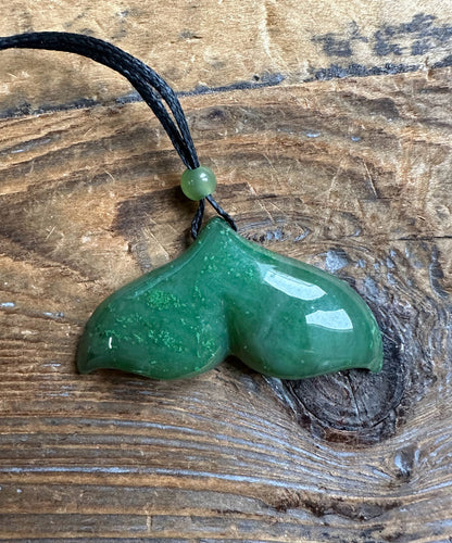 Jade whale tail pendant in green 39mm hanging on a black cord with a green bead.
