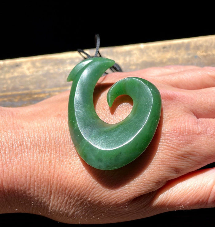 Close-up of a large green jade fish hook pendant resting on a person's hand.