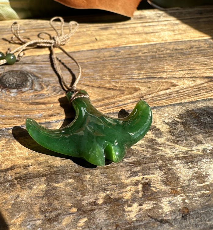 Close-up of green manta ray pendant with cord on weathered wooden surface.