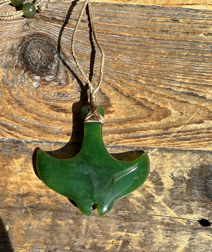Green manta ray pendant on a beige braided cord against weathered wood