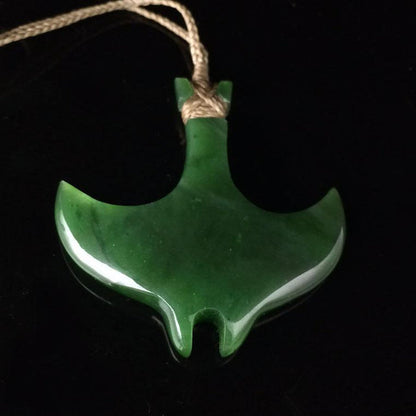 Green jade manta ray pendant suspended on a natural fiber cord against a black background