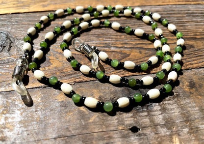 Jade and bone eyeglass holder with white bone beads green jade rounds and black spacers on a rustic wood surface.