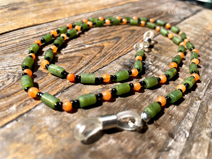 Beaded mask eyeglass holder in jade and carnelian with green cylindrical beads orange rounds black spacers and metal clasp.
