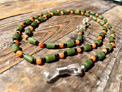 Beaded mask eyeglass holder in jade and carnelian with green cylindrical beads orange rounds black spacers and metal clasp.
