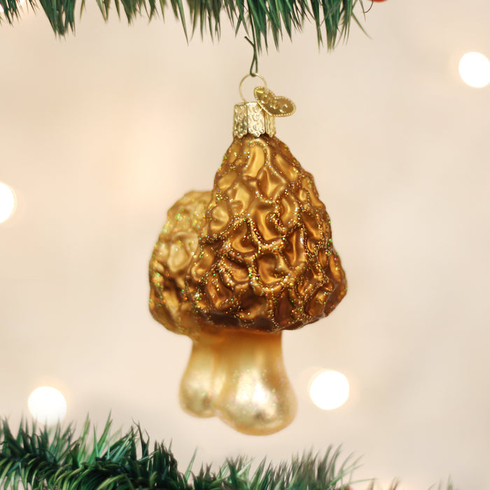 A gold, textured mushroom-shaped ornament hangs from a green Christmas tree branch with a blurred, light-filled background.