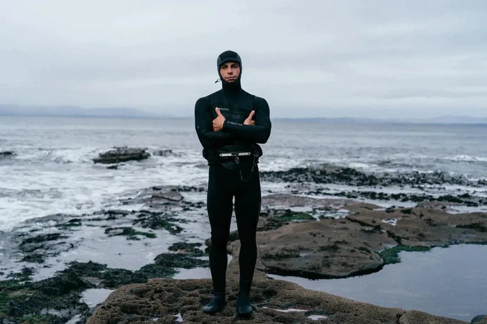 Mystic wetsuit with hood, black fullsuit for watersports, standing on rocky coast near Whitstable