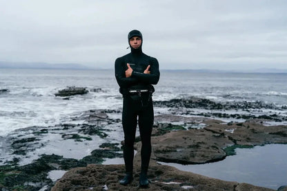 Mystic wetsuit with hood, black fullsuit for watersports, standing on rocky coast near Whitstable