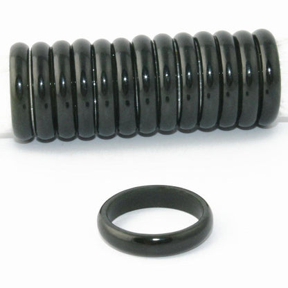 Row of glossy black jade narrow band rings aligned along a rod with one ring lying in front