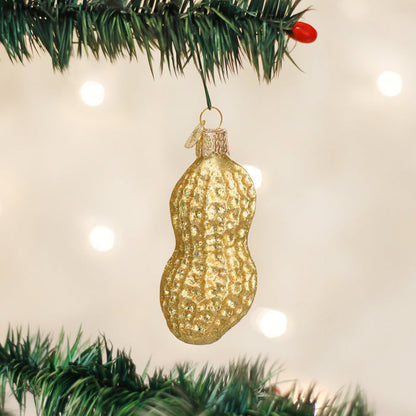 A gold peanut-shaped ornament hangs from a green Christmas tree branch, with blurred white lights in the background.