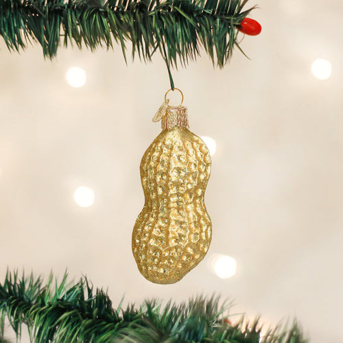 A gold peanut-shaped ornament hangs from a green Christmas tree branch, with blurred white lights in the background.