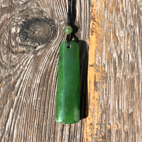 Green cylindrical jade pendant on a black cord with a small green bead