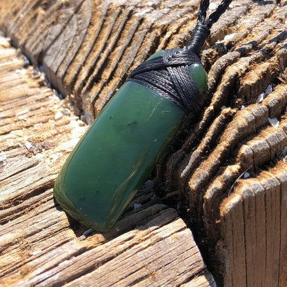 Green jade pendant wrapped in black cord resting on weathered wood.