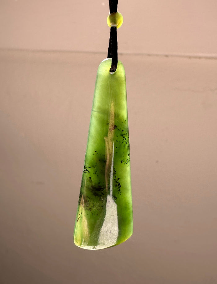 Long green jade drop pendant with a hole at the top, hanging on a black cord with a small yellow bead