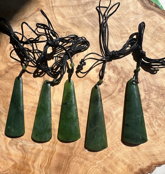 Row of green jade drop pendants on black cords with small beads, laid on a wooden surface.