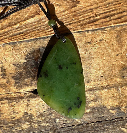 Close-up of the green jade pendant on a black cord resting on wood, showing darker green spots.