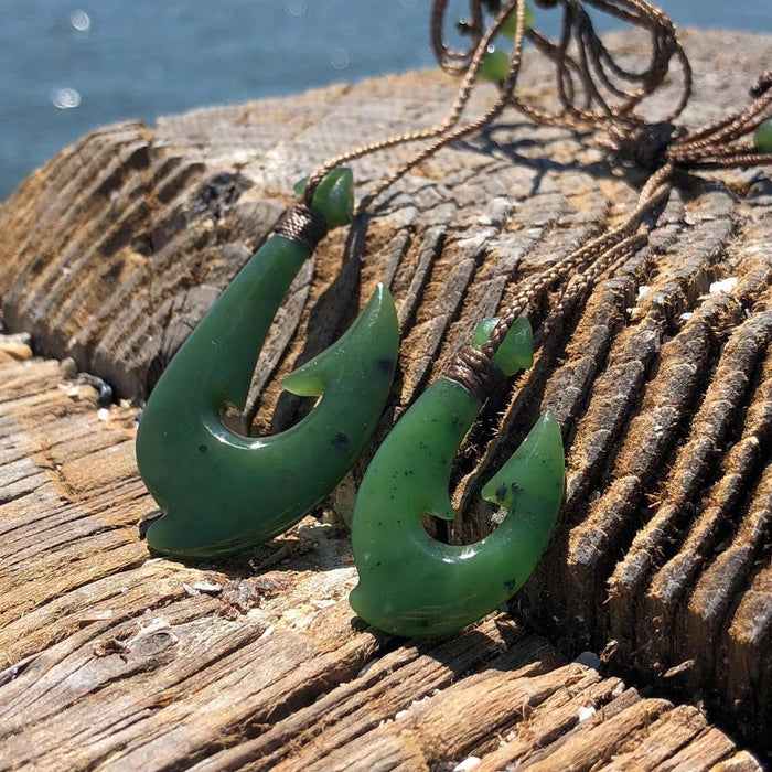 Close up of two green jade fish hook pendants with braided cords on weathered wood surface