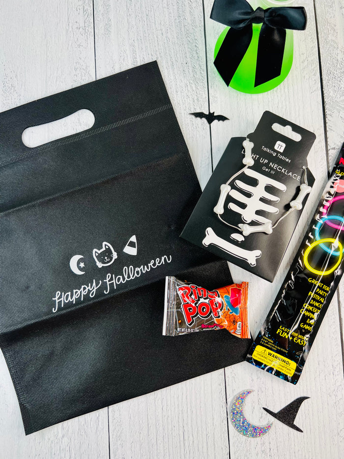 Halloween-themed items including a black bag with 'Happy Halloween' text, a skeleton necklace, and candy on a light wooden surface.