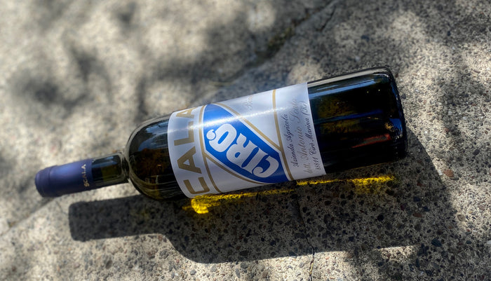 Scala Ciro wine bottle on pavement, blue label on side, dark glass