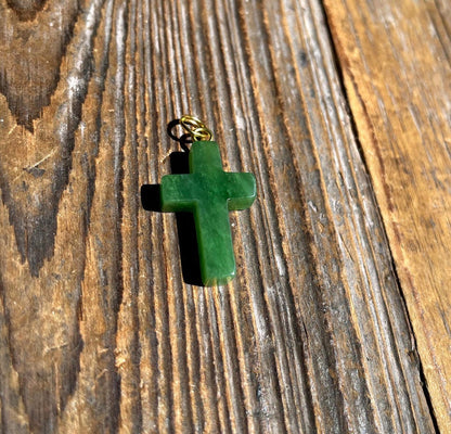 Close up of jade cross pendant on a rustic wood surface with chain