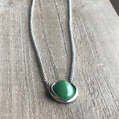 Stainless steel necklace with a green jade pendant resting on a wood surface