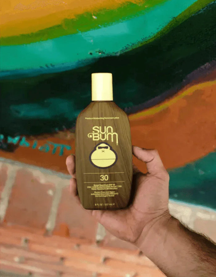 Sun Bum Original SPF 30 sunscreen lotion bottle held in hand with colorful background