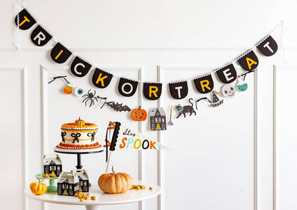 Halloween-themed decor with a 'Trick or Treat' banner, cake, and small houses on a white shelf.